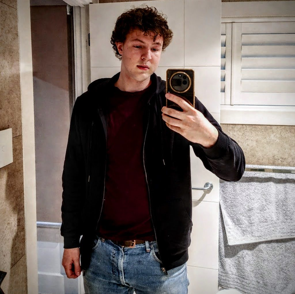 Oakley taking a mirror selfie in a black hoodie and jeans.