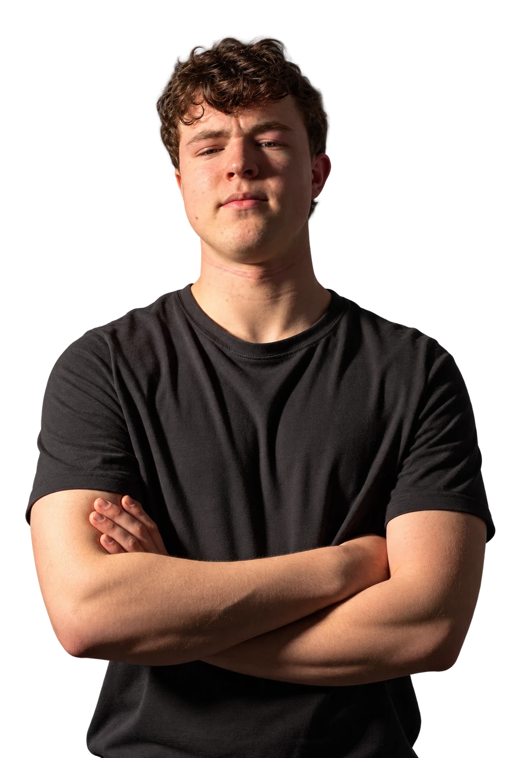 Oakley Jenke standing arms-crossed in a black t-shirt, lit from the side.